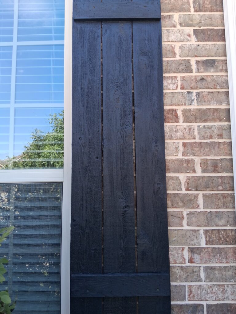 Close-up of a freshly painted black wood shutter against brick siding